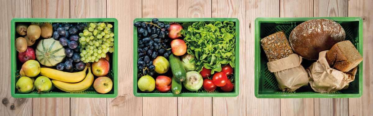 KI generiert: Drei grüne Kisten mit Obst, Gemüse und Brot auf Holzuntergrund.