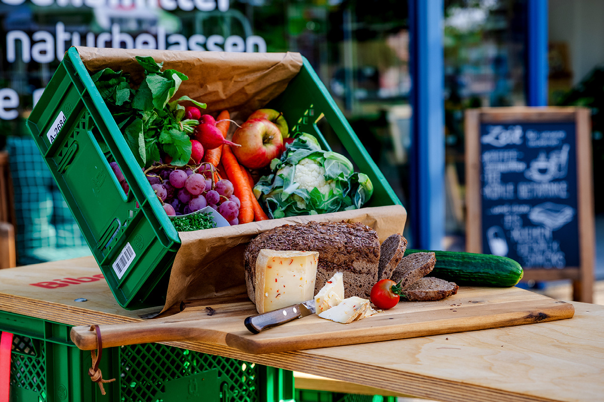 KI generiert: Eine Gemüsekiste mit Brot, Käse und Gemüse auf einem Tisch.