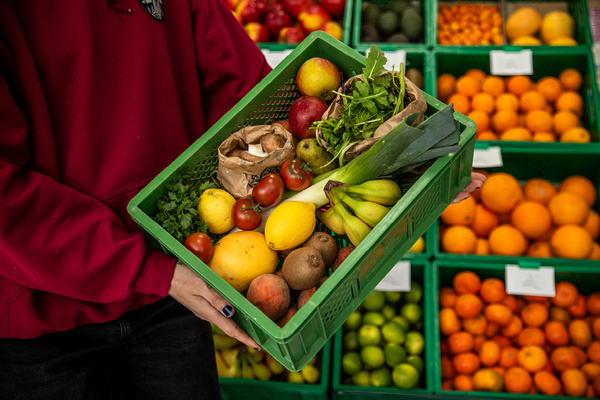 KI generiert: Eine Person hält eine grüne Kiste mit verschiedenen Früchten und Gemüse.