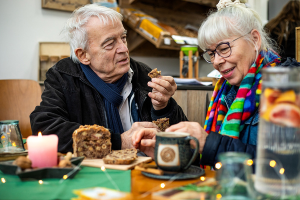 KI generiert: Zwei Personen genießen Gebäck und warme Getränke an einem dekorierten Tisch mit Kerze im Vordergrund.